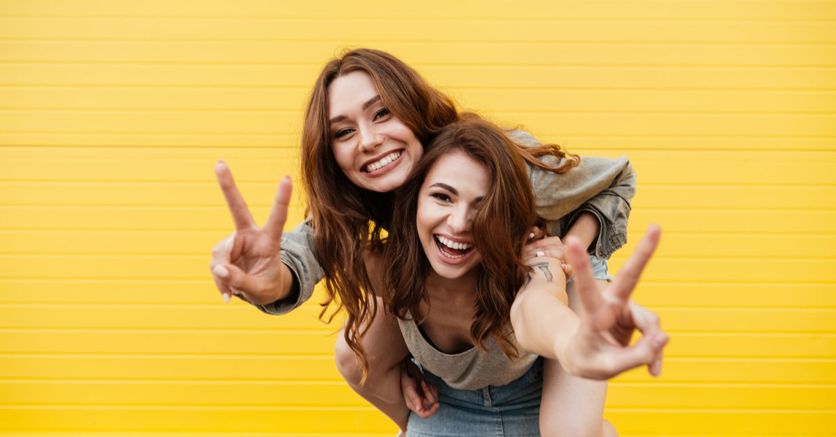 two happy young friends smiling at the camera and making peace signs with their hands